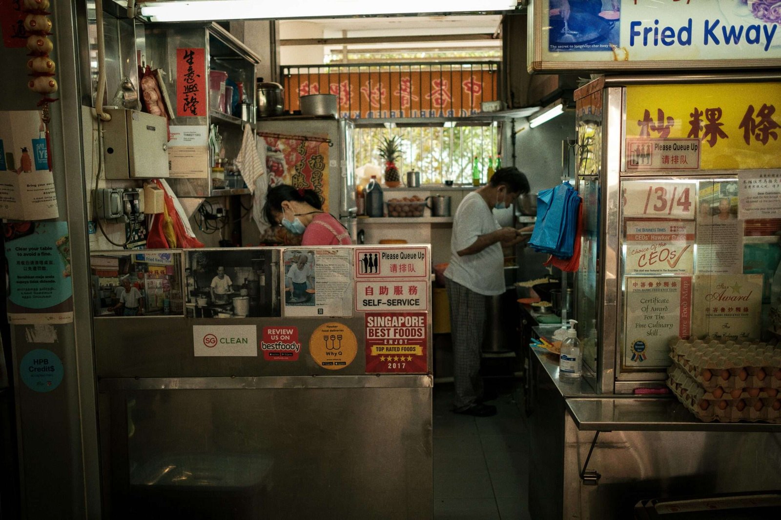pexels-photo-13967613-13967613 A bustling hawker stall in Singapore with staff preparing food in a vibrant setting.