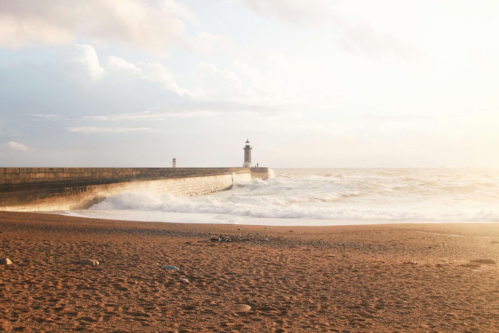 Captivating view of Porto's lighthouse by the ocean at sunset with waves crashing on the shore.